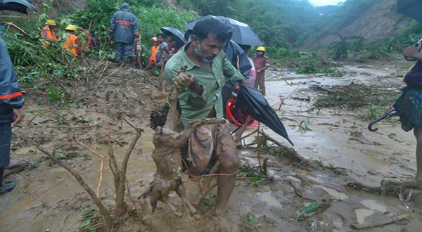 A man carries the carcass of a goat as rescuers search amid the mud after a landslide